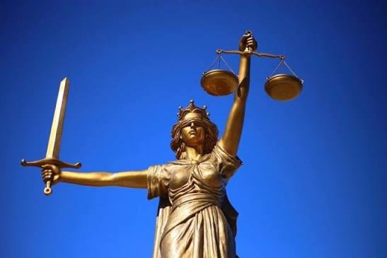 Statue de la justice dorée tenant une balance et une épée, sur fond de ciel bleu